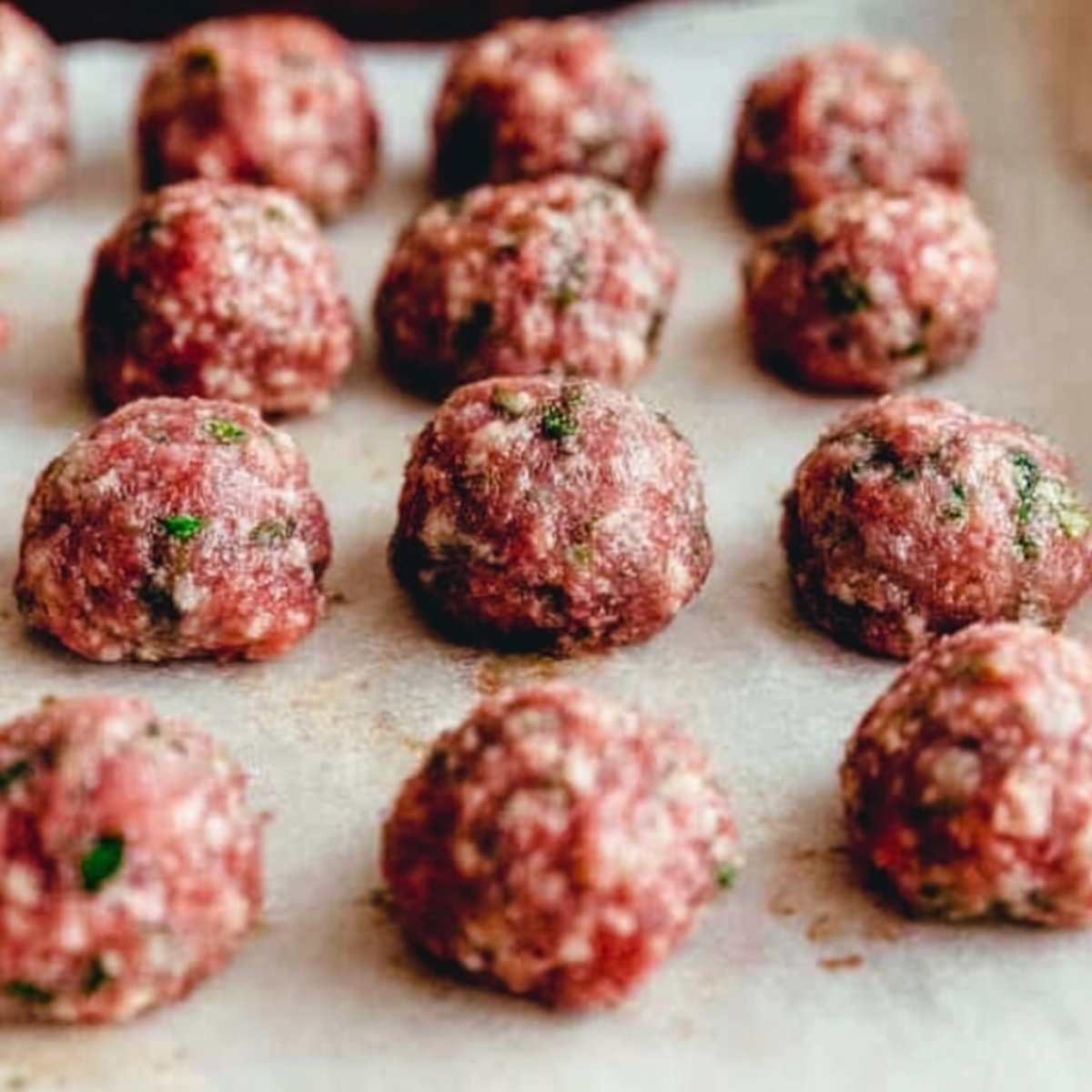 Close up of raw, freshly shaped meatballs arranged neatly on a parchment paper-lined tray, ready for cooking.