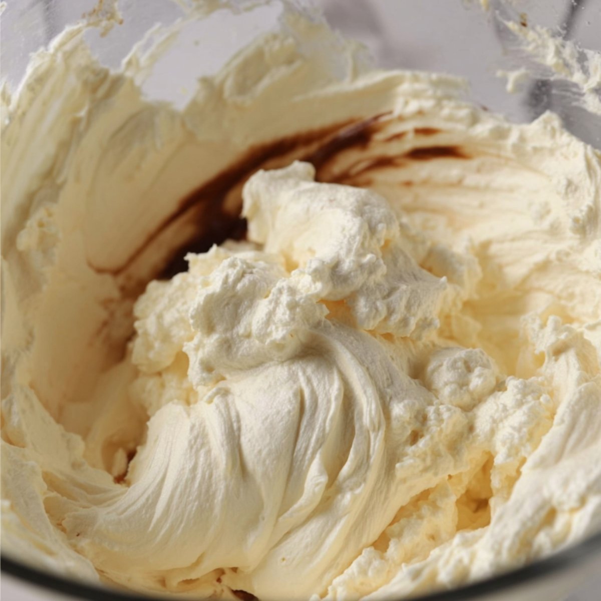 Close-up of a mixing bowl filled with smooth, whipped cream cheese and vanilla extract being blended into a creamy cheesecake filling.