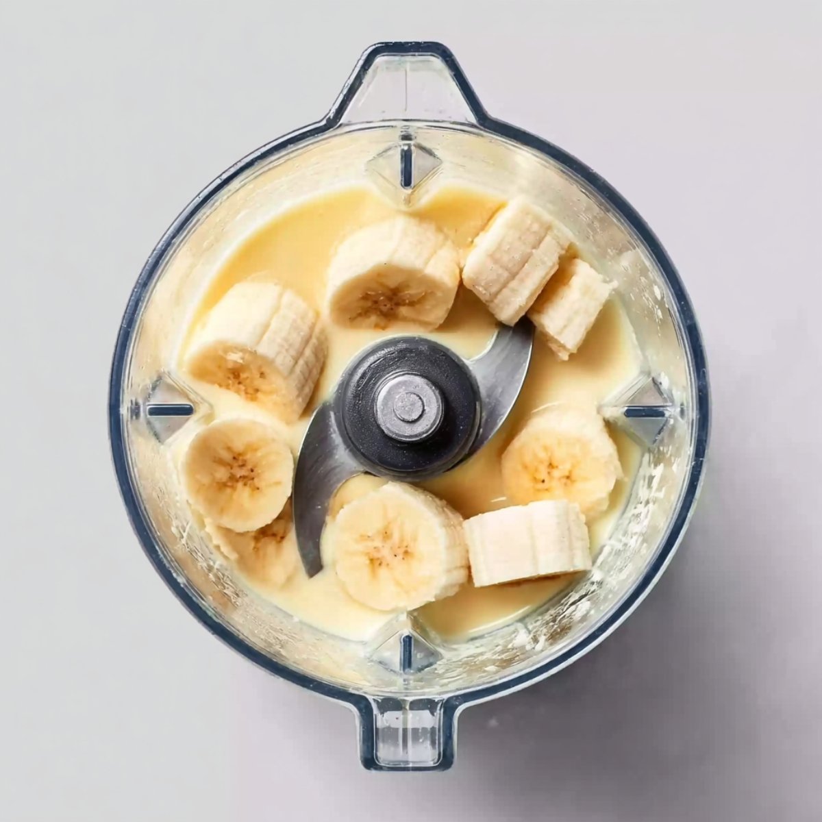 Banana slices and creamy liquid inside a blender, ready to be blended.