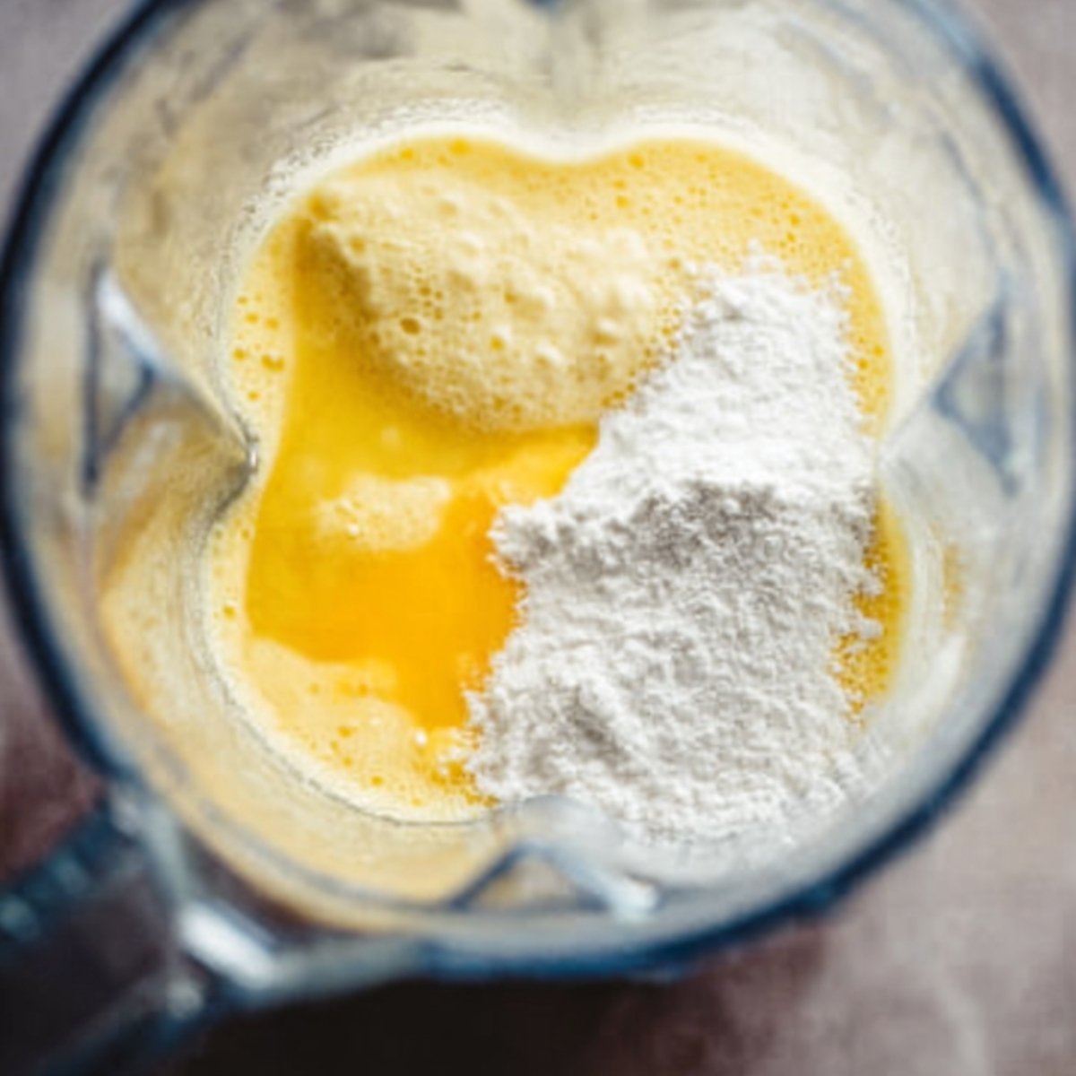 Close up of a blender with ingredients for crepe batter: eggs and flour, ready to be blended into a smooth, pourable mixture.
