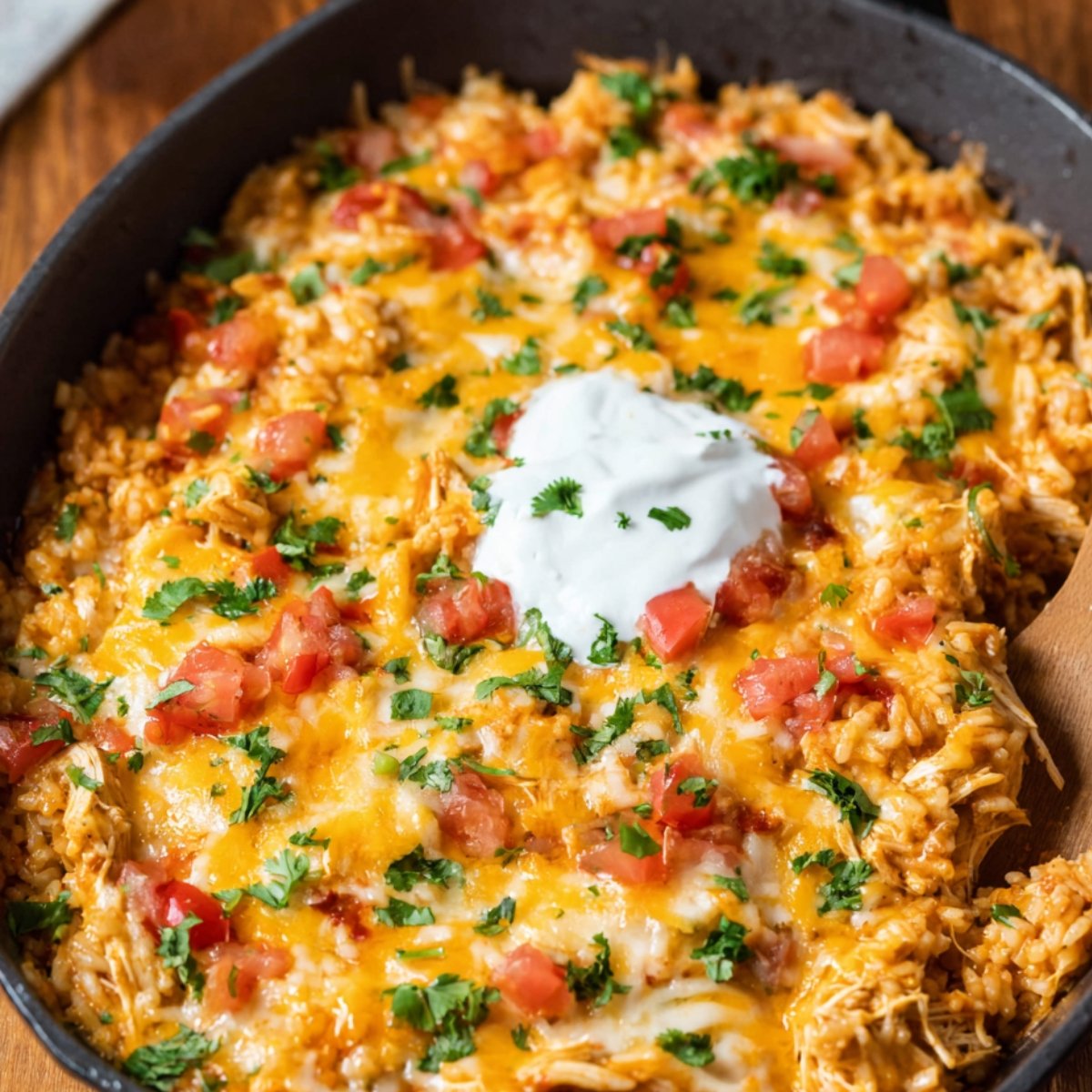A skillet filled with chicken fajita casserole, topped with melted cheese, fresh cilantro, and diced tomatoes, ready to be served.