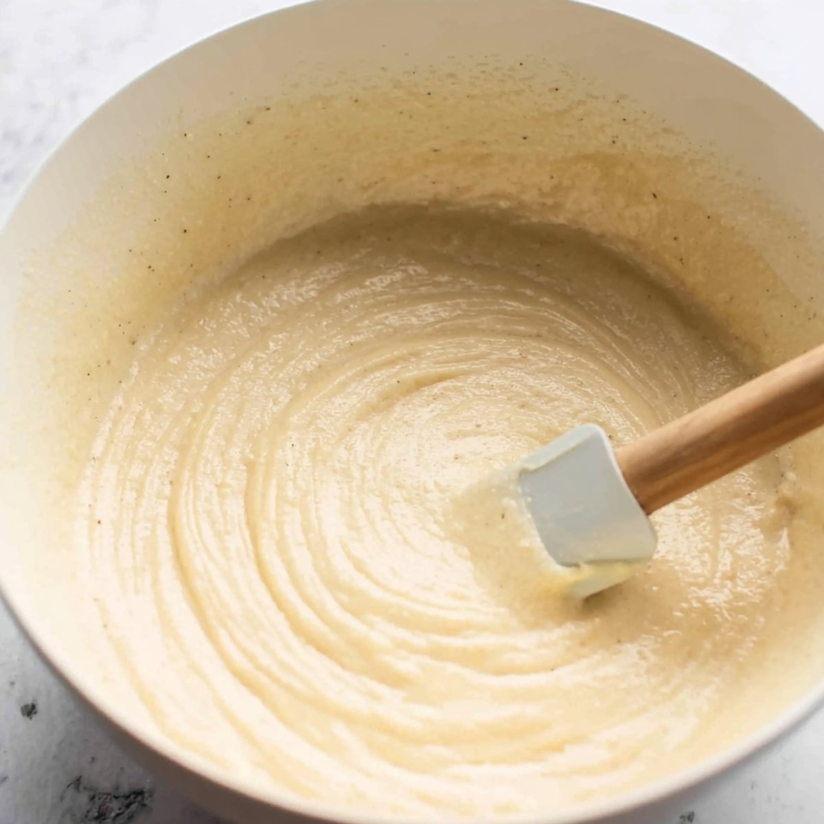 A bowl of pancake batter being stirred with a spatula.