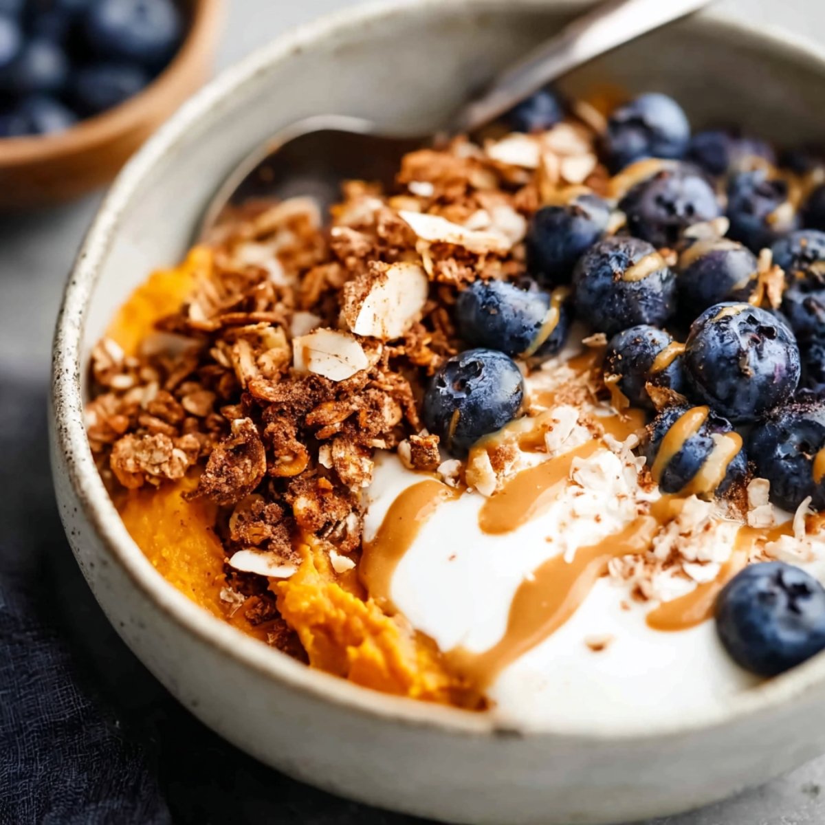 A beautifully arranged sweet potato breakfast bowl topped with creamy yogurt, fresh blueberries, granola, and a drizzle of nut butter, perfect for a nutritious start to the day.