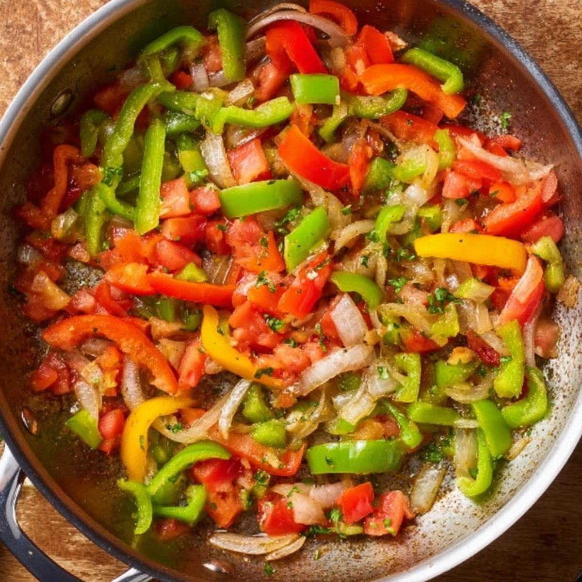 Close up of sautéed bell peppers, onions, and tomatoes in a skillet, with vibrant colors and fresh herbs, ready to be added to a dish.