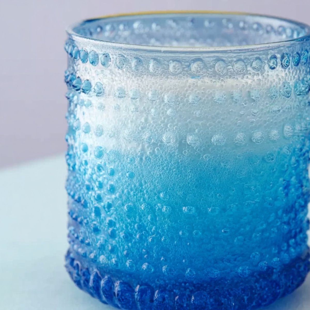 Close up of a textured blue drink in a decorative glass, showcasing a beautiful gradient of blue hues. The drink appears frosty, with condensation on the glass, evoking a refreshing, chilled vibe.