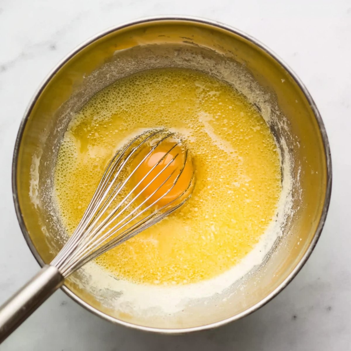 A bowl of whisked wet ingredients, including an egg, with a whisk inside.