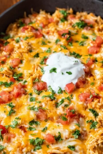 A skillet filled with chicken fajita casserole, topped with melted cheese, fresh cilantro, and diced tomatoes, ready to be served.