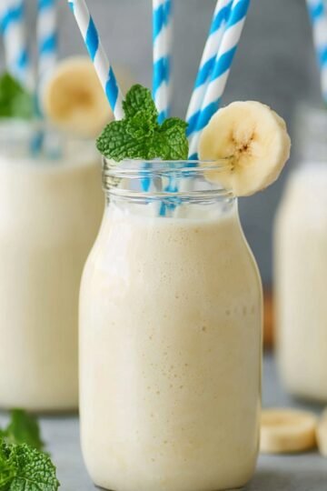 Korean Banana Milk served in glass bottles with blue striped straws, garnished with mint and banana slices.