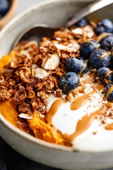 A beautifully arranged sweet potato breakfast bowl topped with creamy yogurt, fresh blueberries, granola, and a drizzle of nut butter, perfect for a nutritious start to the day.